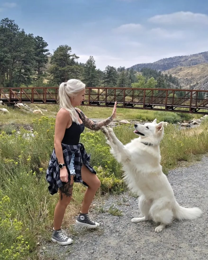 Nicole high-fiving Neo, her white Berger Blanc Suisse, on a mountain trail